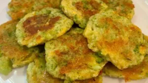 Crispy broccoli cheddar fritters on a plate, garnished with herbs.