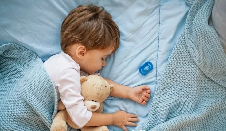 Toddler sleeping comfortably in their own bed with a soft blanket