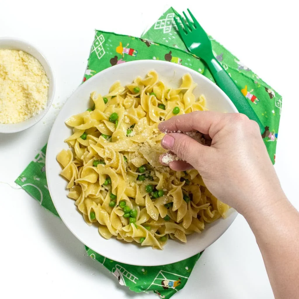 Bowl of kid-approved butter noodles with peas and parmesan cheese
